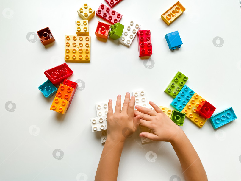 Скачать Ребенок играет с разноцветными строительными блоками на белом фоне. Вид сверху фотосток Ozero
