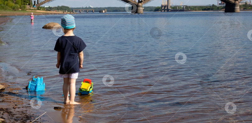Скачать Маленький мальчик в синей футболке и полосатой шляпе стоит в воде.Летние каникулы на берегу реки. Место для текста фотосток Ozero