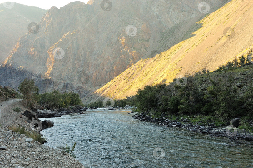 Скачать Небольшая речка со скалистыми берегами течет по дну глубокого каньона в тени гор и заходящего солнца. фотосток Ozero