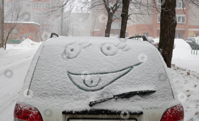 Скачать Забавное лицо, сделанное из снега на окне машины. Автомобиль на городской улице, покрытой снегом зимой фотосток Ozero