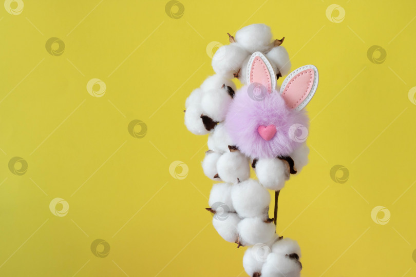 Скачать Красивые белые хлопковые цветы и маленький пушистый сиреневый игрушечный кролик на желтом фоне. Пасхальная концепция. место для вашего текста фотосток Ozero