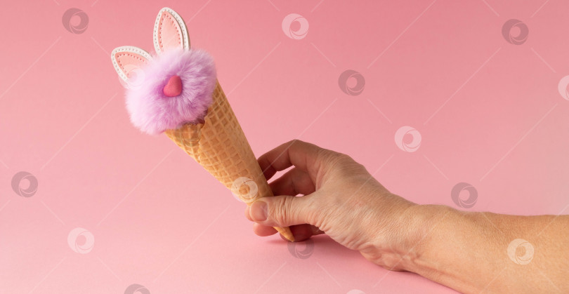 Скачать Абстрактный розовый фон. Рука с пушистым сиреневым кроликом в вафельном рожке. Концепция любви, поздравительная открытка ко Дню святого Валентина и Пасхе фотосток Ozero