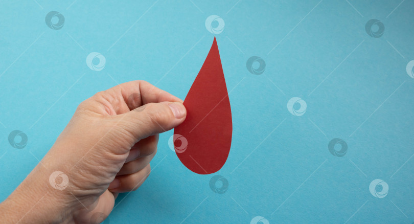 Скачать Концепция Всемирного дня донора крови и борьбы с гемофилией. Красная бумажная капля крови в руке на синем фоне фотосток Ozero