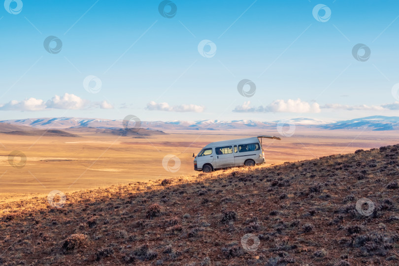 Скачать Старый белый фургон с открытым задним багажником, припаркованный на крутом горном склоне на фоне осенней степи, экстремальное путешествие по бескрайним просторам. фотосток Ozero