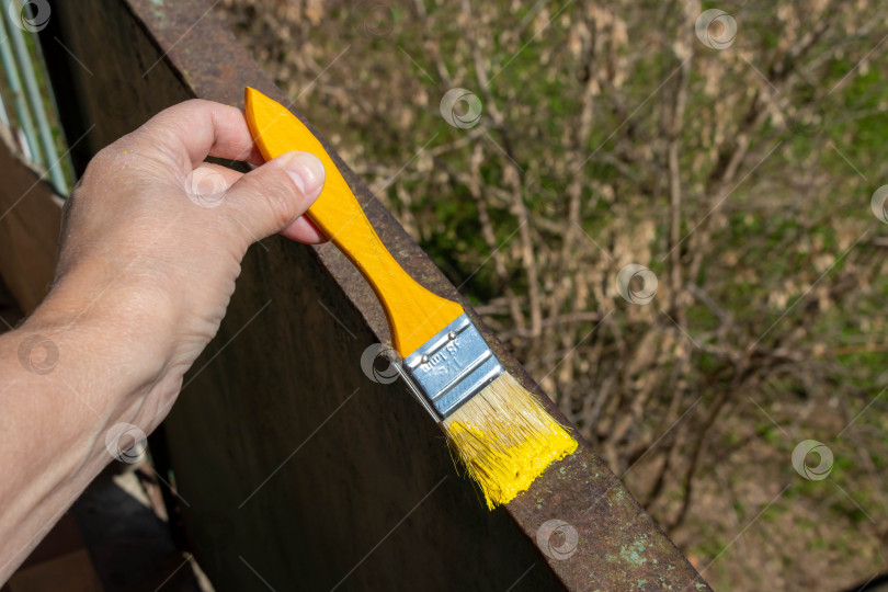 Скачать Рука с желтой кистью рисует ржавые металлические перила на балконе в солнечный день. Сделай сам фотосток Ozero