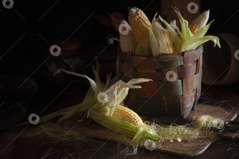 Скачать Свежие кукурузные початки в корзинке на деревянном столе в винтажной кухне moody фотосток Ozero