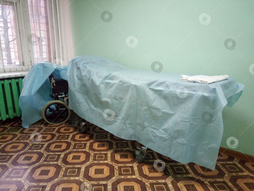 Скачать Кровать-каталка, покрытая синей простыней, или носилки на колесиках для транспортировки лежачих пациентов по больничному коридору фотосток Ozero