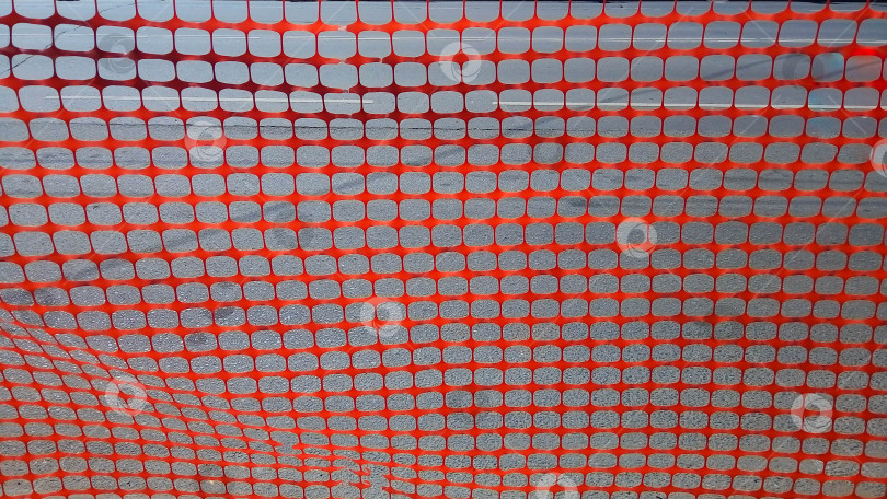 Скачать Декоративный забор из красной пластиковой сетки на фоне серой бетонной дороги фотосток Ozero