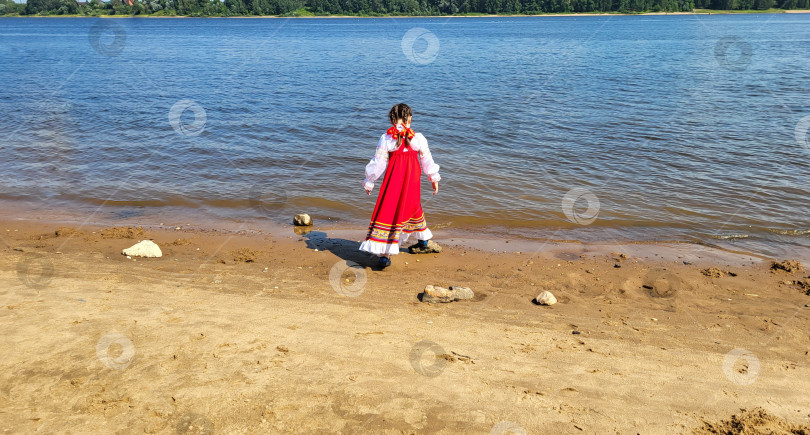 Скачать Маленькая девочка в красном винтажном сарафане стоит и смотрит на реку фотосток Ozero