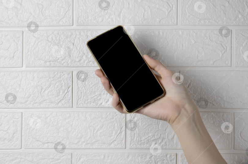 Скачать Рука, держащая новый смартфон на фоне белой кирпичной стены фотосток Ozero