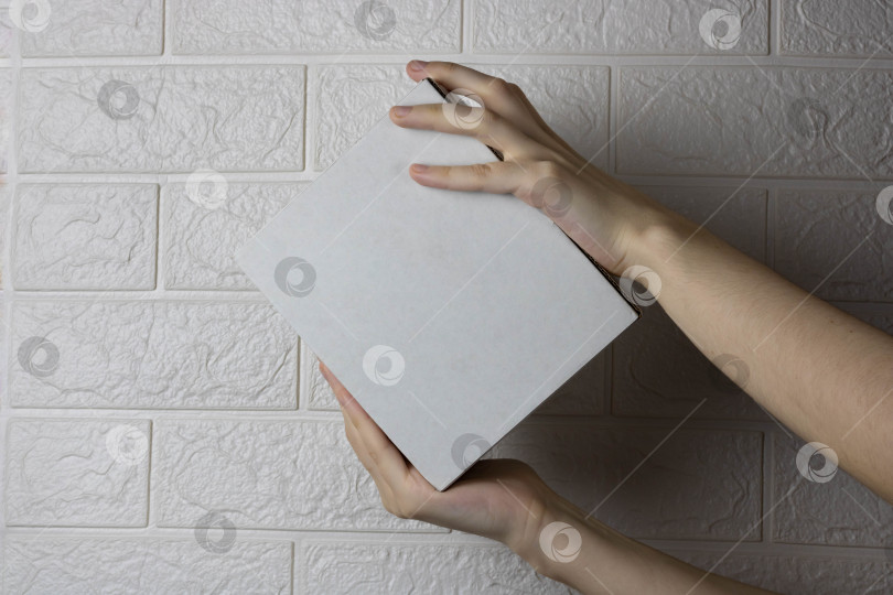 Скачать Руки с пустой картонной коробкой на фоне светлой кирпичной стены фотосток Ozero