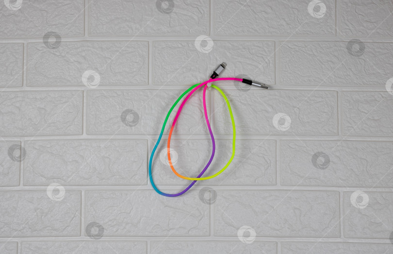 Скачать Разноцветный радужный провод для зарядки смартфона висит на белой кирпичной стене фотосток Ozero