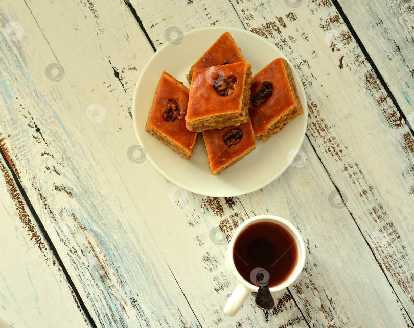 Скачать Чашка горячего черного чая и тарелка с кусочками свежей медовой пахлавы на столе из светлого дерева. фотосток Ozero