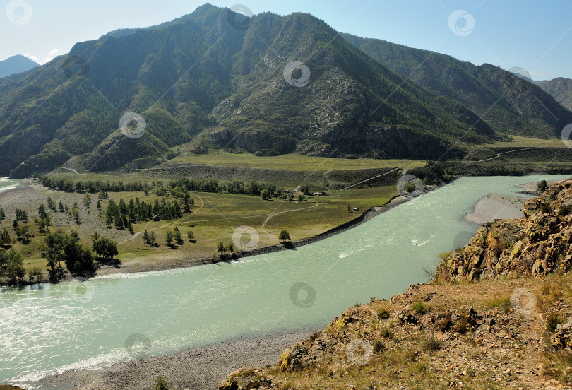 Скачать Русло широкой бирюзовой реки, текущей вокруг горного хребта по долине в лучах заходящего летнего солнца. фотосток Ozero