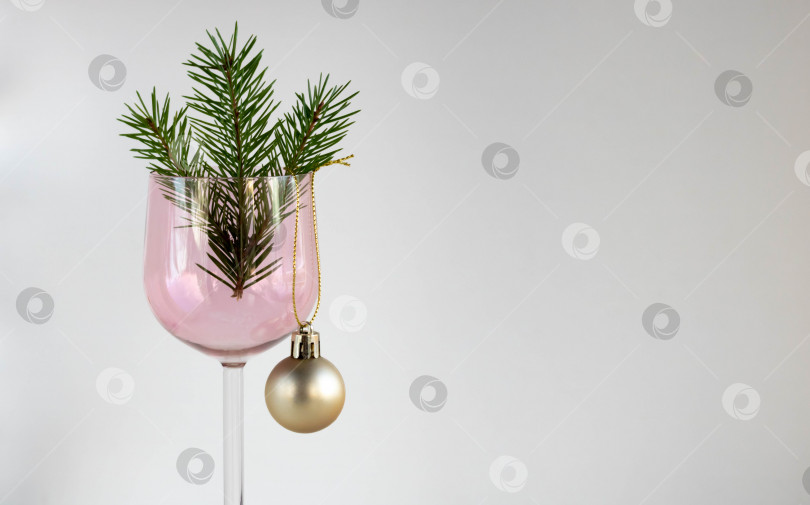 Скачать Бокал для вина из розового стекла с еловой веточкой и игрушечным золотым шаром на белом фоне. Концепция Рождества и Нового года фотосток Ozero