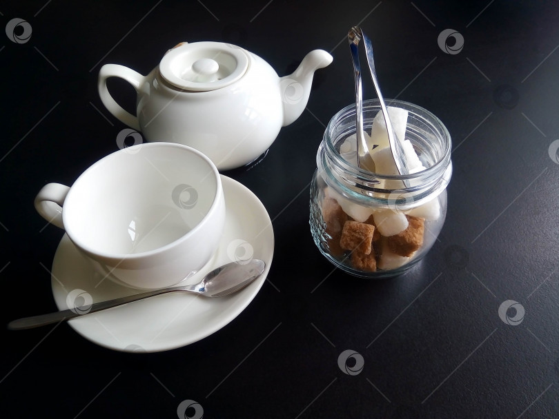 Скачать Белая чашка с блюдцем, баночка сахара и заварочный чайник, выделенные на черном фоне фотосток Ozero