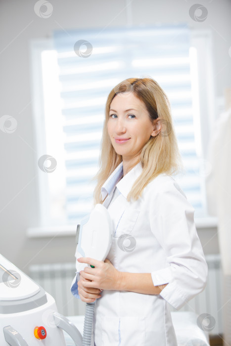 Скачать Фотография молодой красивой женщины-врача, стоящей в кабинете дерматолога с инструментом для лазерной эпиляции в руках фотосток Ozero