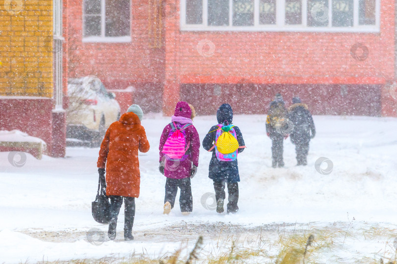 Скачать Снежная буря в городской среде, люди, дети идут домой из школы во время снегопада зимой. фотосток Ozero