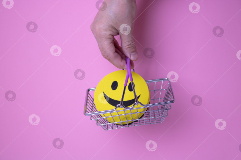 Скачать В руке корзинка с желтым улыбающимся смайликом на розовом фоне фотосток Ozero