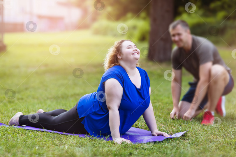 Скачать Молодая блондинка больших размеров выполняет упражнение на спортивной площадке с тренером. Концепция здорового образа жизни фотосток Ozero