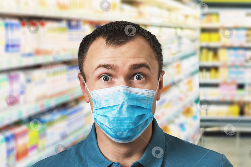 Скачать Удивленный мужчина в медицинской маске на фоне прилавка супермаркета. Концепция повышения цен в магазинах во время карантина из-за пандемии коронавируса фотосток Ozero