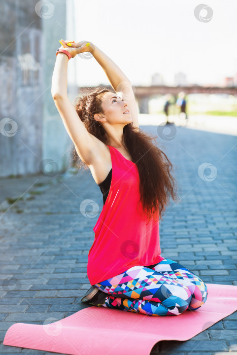 Скачать Шатенка выполняет упражнение на гимнастическом коврике на набережной теплым солнечным летним утром фотосток Ozero