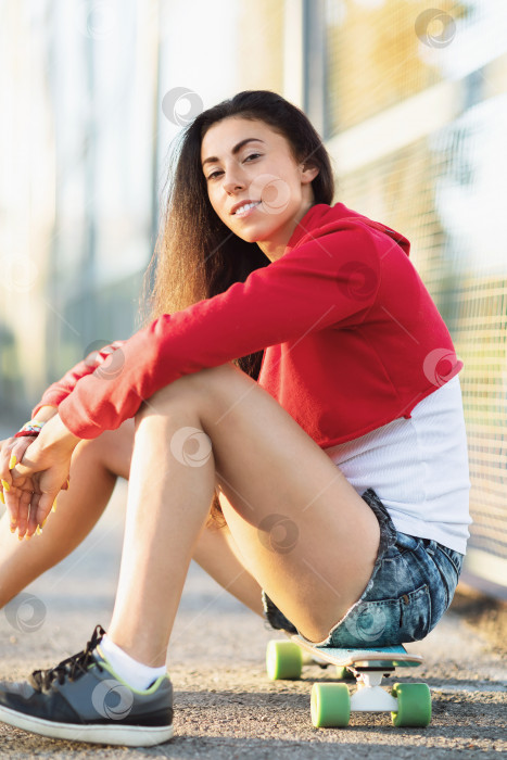 Скачать Молодая женщина сидит на скейтборде на спортивной площадке летним солнечным вечером фотосток Ozero