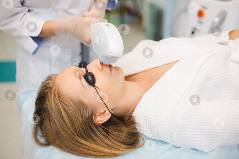 Скачать Крупный план лица молодой женщины во время проведения косметологом процедуры лазерной эпиляции нежелательных волос на лице и верхней губе в салоне красоты фотосток Ozero