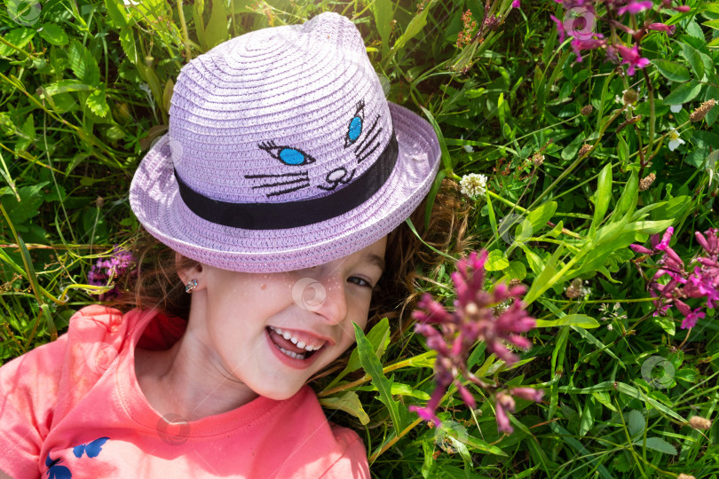 Скачать Портрет ребенка в шляпе с закрытым летом лицом, лежащего в траве и полевых цветах. Шляпа с глазами и ушами, как у кошки, летнее время, свобода фотосток Ozero