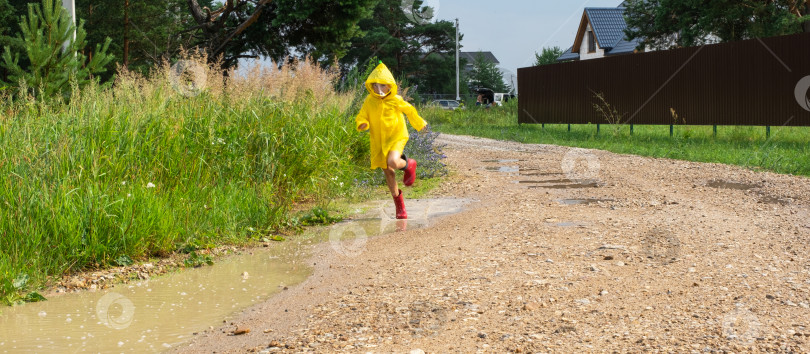 Скачать Девочка в красных резиновых сапогах и желтом дождевике бежит по лужам после дождя в деревне. Летнее время, свобода, детство фотосток Ozero