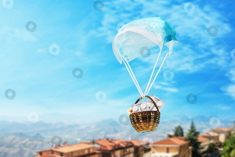 Скачать Медицинская маска в виде парашюта и корзинки с таблетками на фоне неба. Концепция гуманитарной помощи фотосток Ozero
