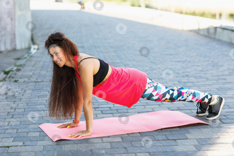 Скачать Молодая женщина занимается спортом на открытом воздухе солнечным летним утром, выполняя упражнение на доске. Концепция здорового образа жизни фотосток Ozero