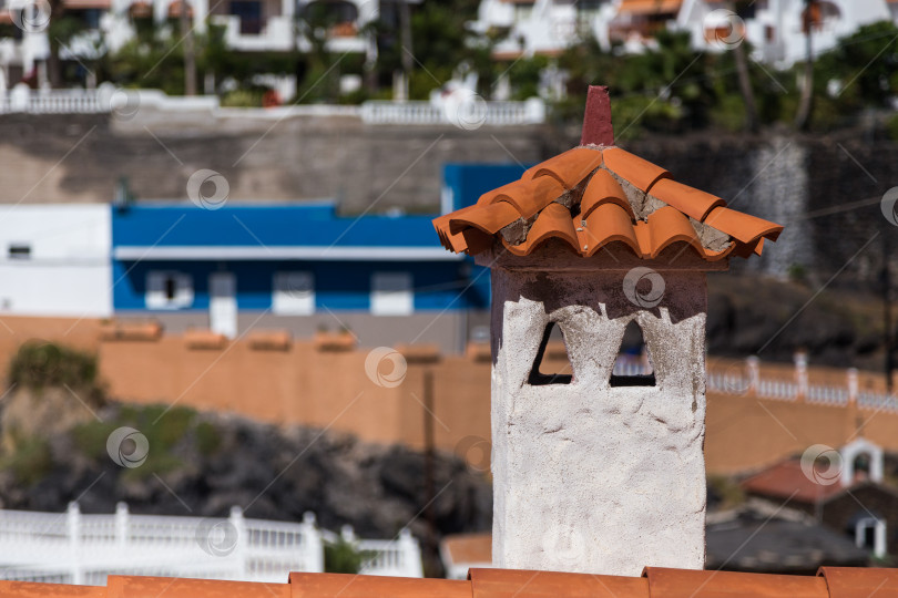 Скачать Оранжевая черепичная крыша с дымоходом в средиземноморском стиле, здания на заднем плане. фотосток Ozero