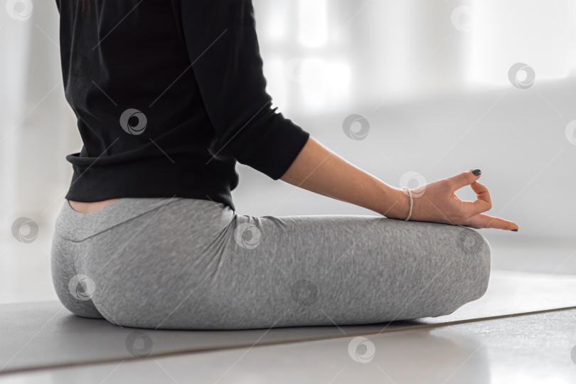 Скачать Медитация во время выполнения позы лотоса. Женщина сидит на сером коврике и практикует йогу в классе. Поза корневой чакры двумя пальцами фотосток Ozero