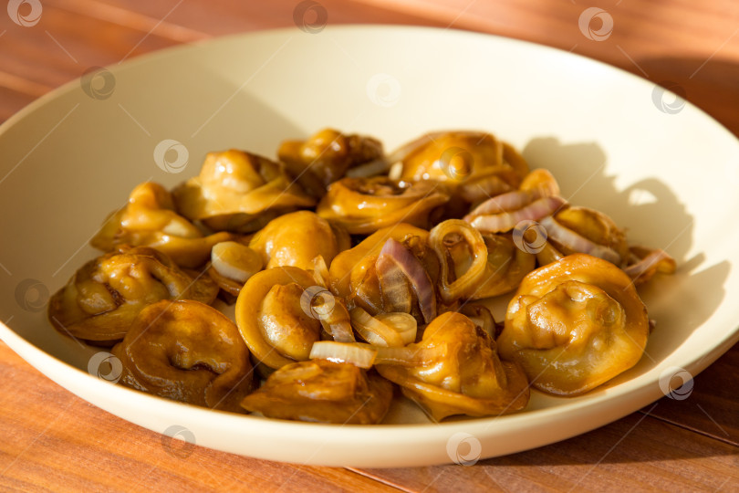 Скачать Пельмени с жареным луком и коричневым соусом в бежевой тарелке на деревянном столе в sunny kitchen фотосток Ozero