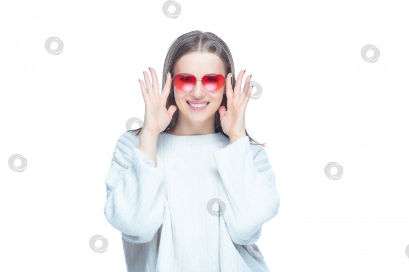 Скачать Студийный портрет симпатичной гламурной женщины, надевающей красные солнцезащитные очки обеими руками возле своего лица, изолированного на белом фоне фотосток Ozero