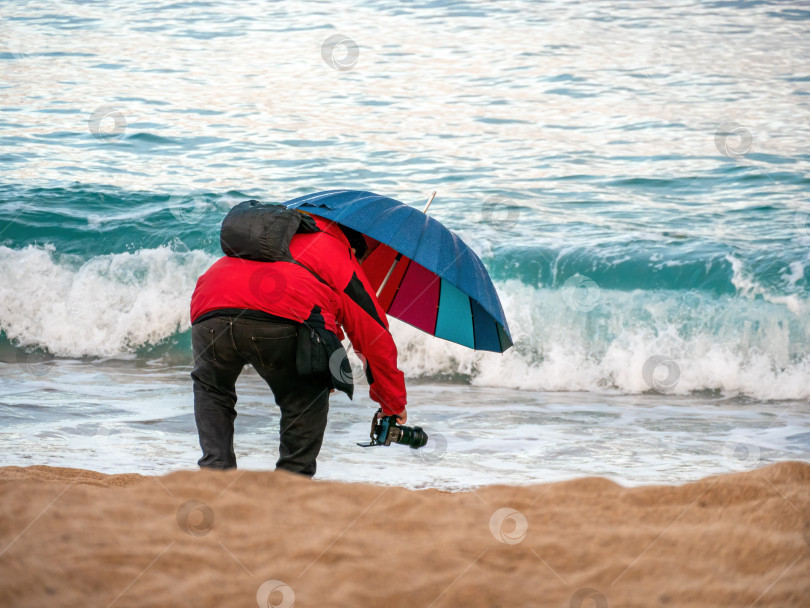 Скачать фотограф с зонтиком под дождем, фотографирует волны фотосток Ozero
