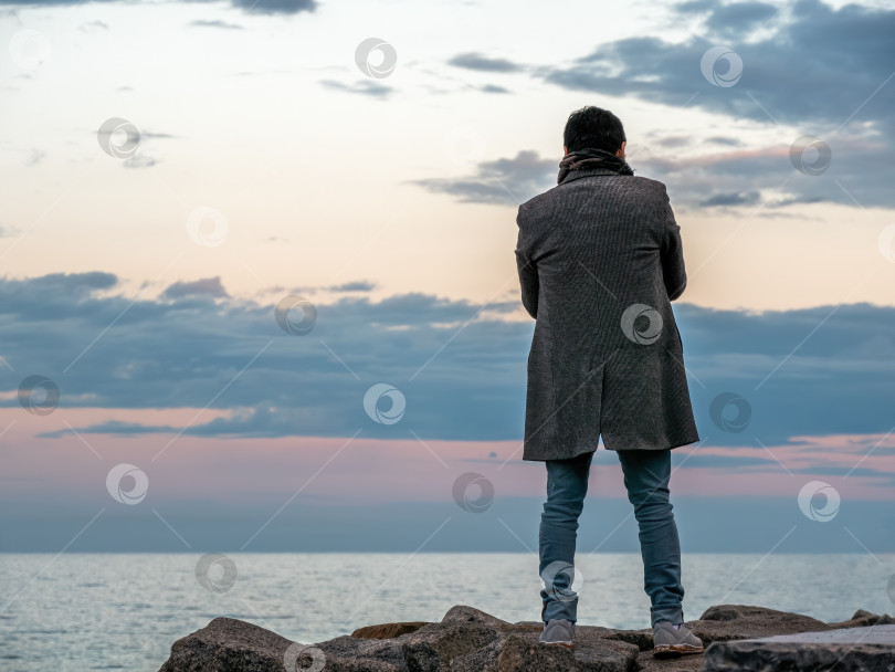 Скачать Мужчина стоит на камнях и смотрит на море на закате фотосток Ozero