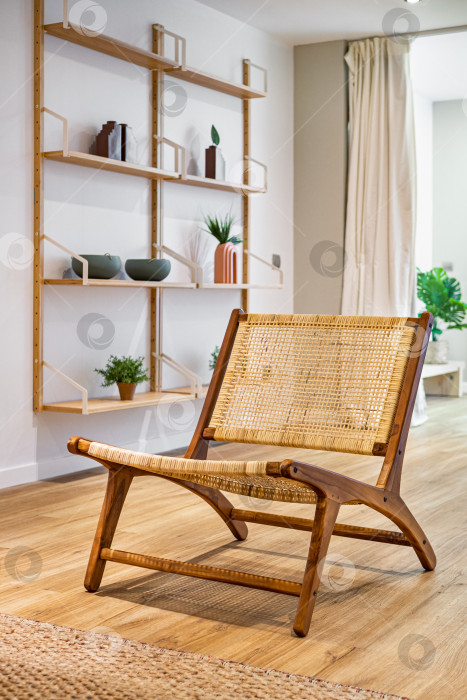 Скачать Современное плетеное кресло, стоящее в гостиной с серой стеной и полками с украшениями. Внутренняя деревянная мебель. фотосток Ozero