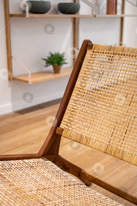 Скачать Деталь спинки современного плетеного кресла, стоящего в гостиной с серой стеной и полками с украшениями и растениями. Внутренняя деревянная мебель фотосток Ozero