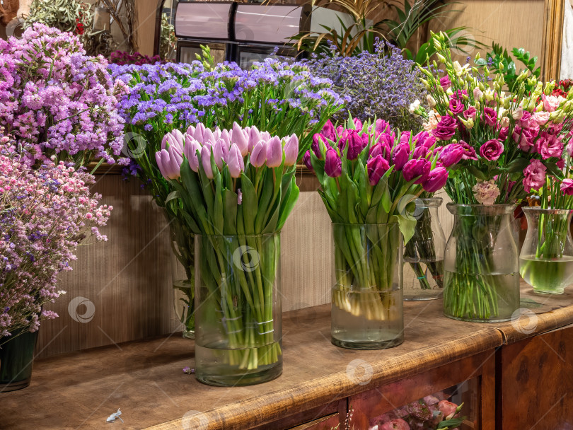Скачать Продаются красивые разноцветные цветы, расставленные в вазах в цветочном магазине. Тюльпаны, розы и лимониум фотосток Ozero