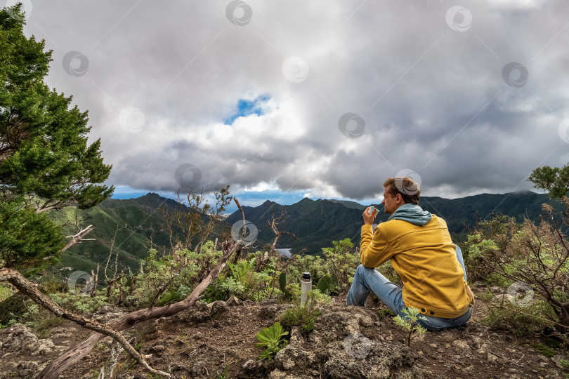Скачать Молодой мужчина-путешественник пьет горячий напиток в горах. Пьет чай или кофе из термоса на природе. фотосток Ozero