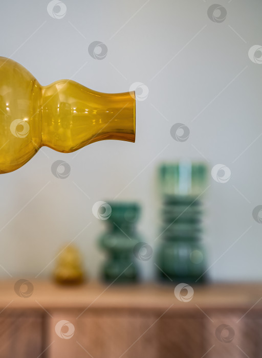 Скачать Горлышко желтой прозрачной бутылки с несколькими вазочками на размытом фоне. Оформление интерьера. фотосток Ozero
