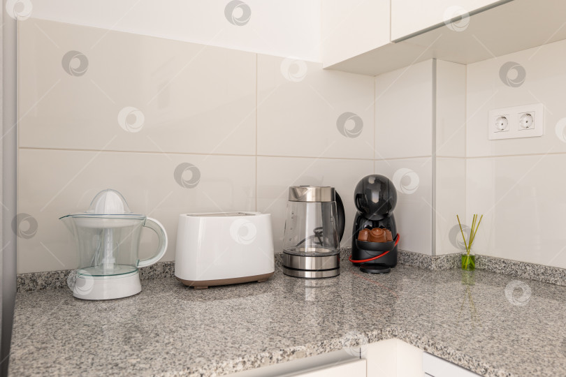 Скачать Крупный план кухонного стола с соковыжималкой и кухонными приборами на фоне белой плитки и кухонных шкафчиков. Концепция домашней утвари и удобных приспособлений для приготовления пищи фотосток Ozero