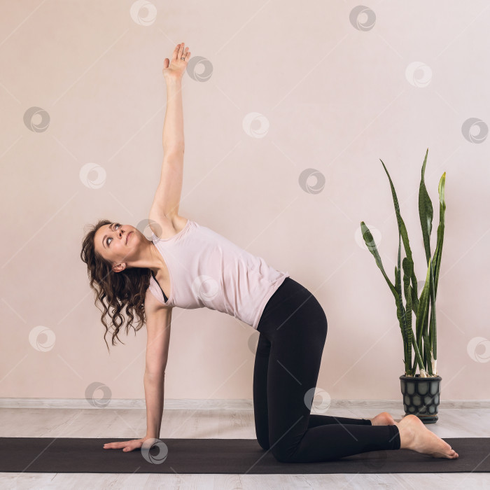 Скачать Женщина, практикующая йогу, выполняющая упражнение гоасана, поза стола для скручивания груди, в студии на коврике у стены фотосток Ozero