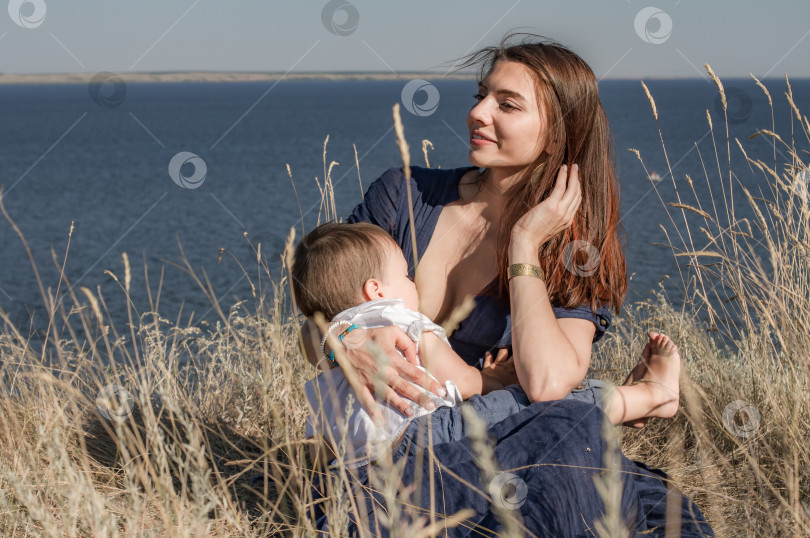 Скачать Молодая счастливая мать кормит ребёнка грудью в поле. фотосток Ozero