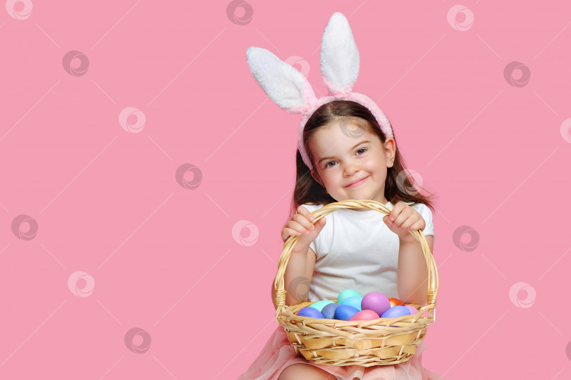 Скачать Счастливая улыбающаяся девушка с повязкой на голове пасхального кролика и корзинкой с яйцами фотосток Ozero