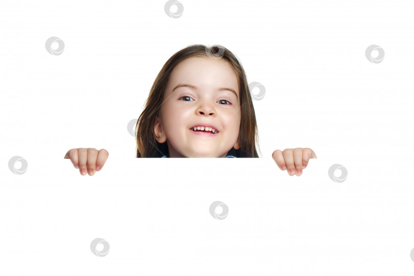 Скачать Улыбающаяся маленькая девочка прячется за пустой доской в белой студии фотосток Ozero