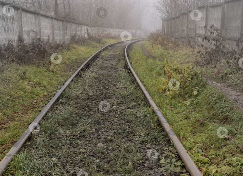 Скачать Старая железная дорога, ведущая к полузаброшенному закрытому объекту осенью в тумане. фотосток Ozero