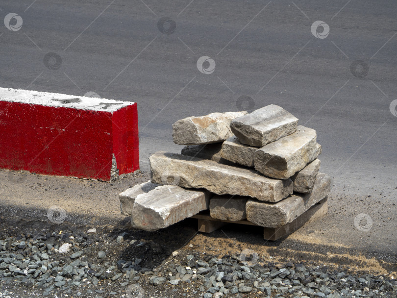 Скачать Старые использованные бордюры сложены на краю асфальтированной дороги рядом с бордюрным камнем, выкрашенным в красный цвет. Дорожное строительство. Замена бордюров. фотосток Ozero